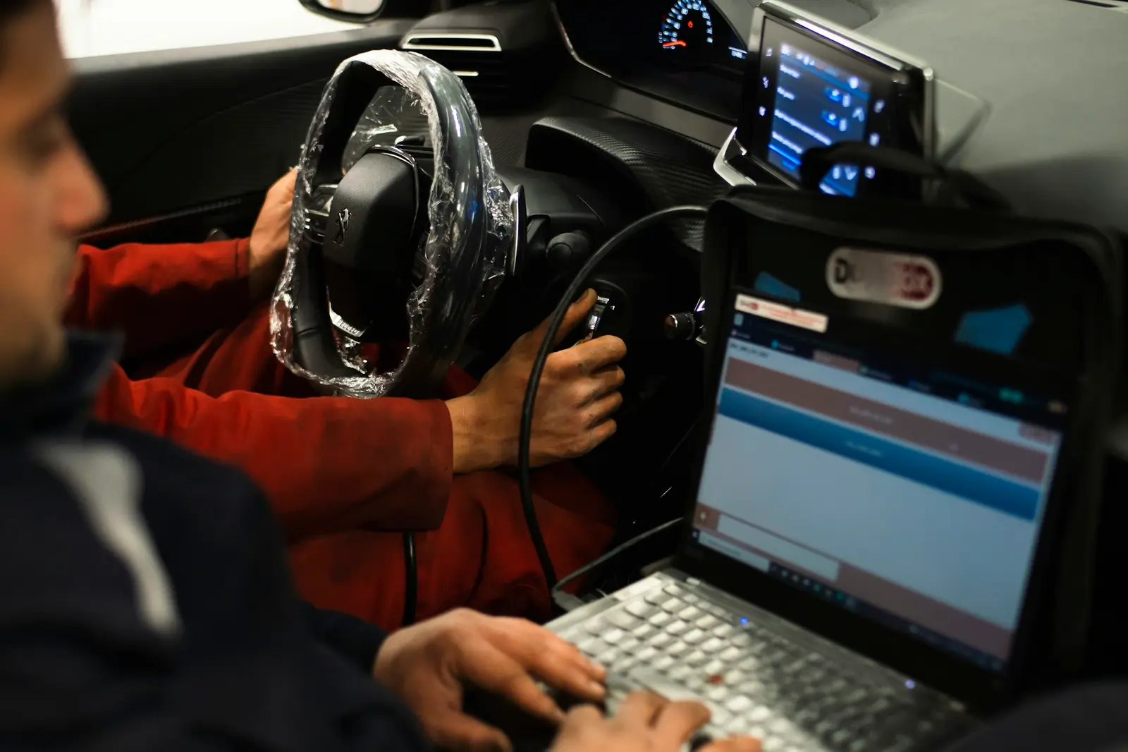 Technician running engine diagnostics on a laptop plugged into a car