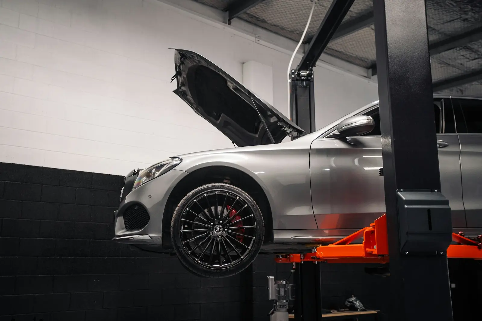 Silver car raised on a two-post lift in a garage workshop